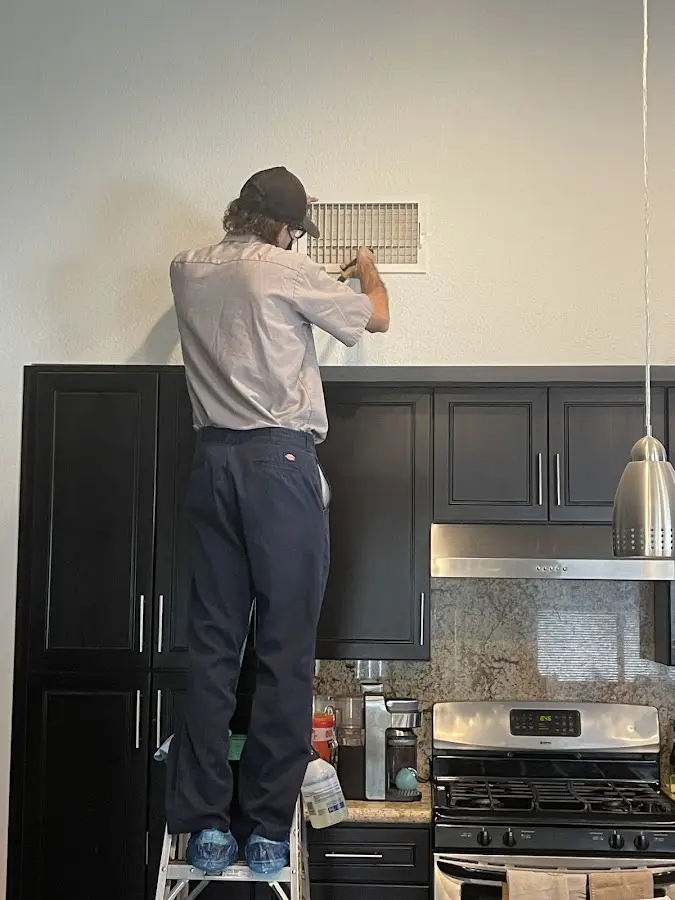 Technician inspecting an air vent during HVAC service in Kenmore